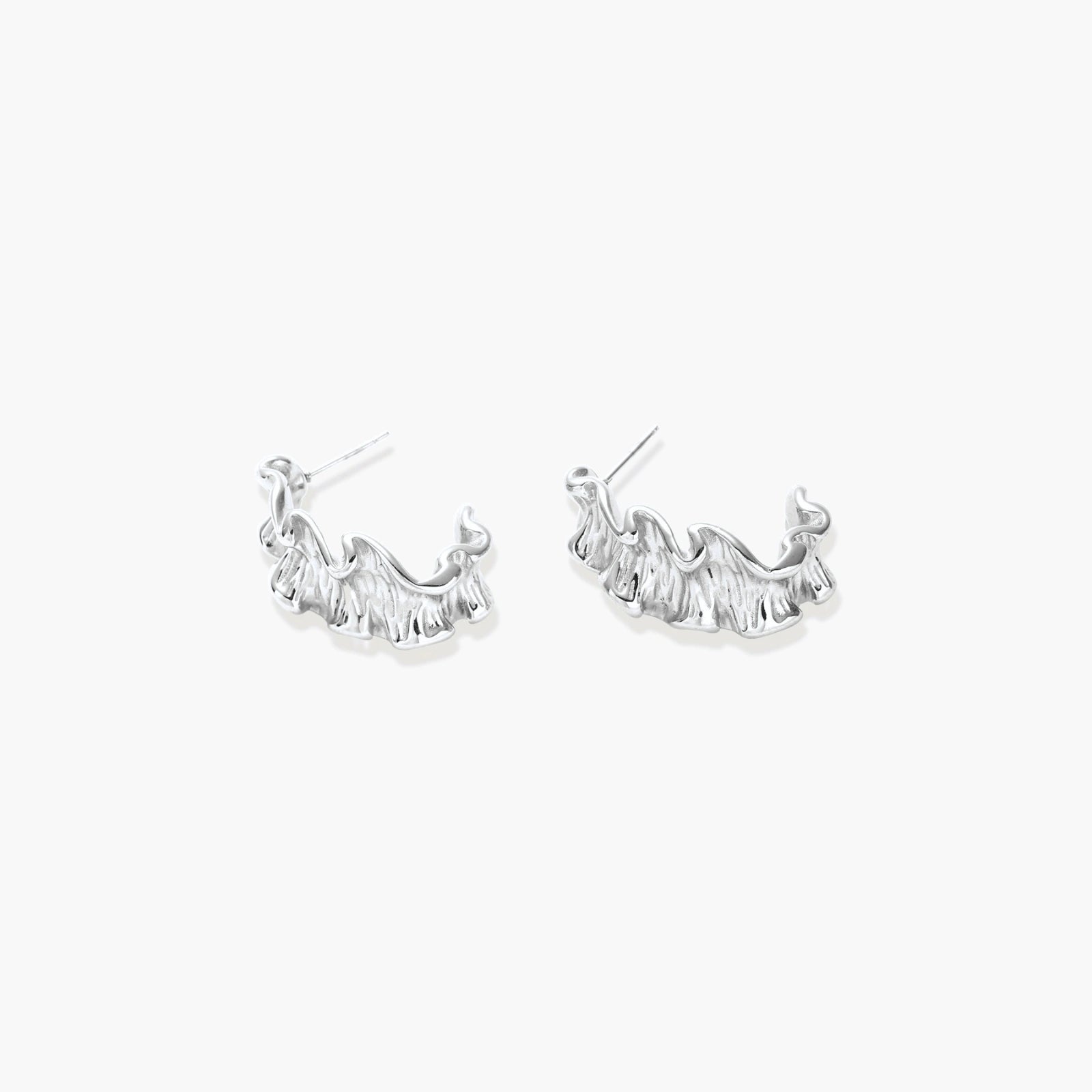 Textured white gold-plated hoop earrings with flowing wave pattern against cream background, showing dimensional rippled surface.