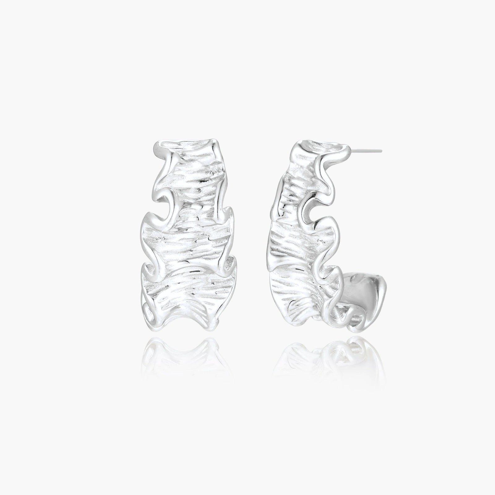 Textured white gold-plated hoop earrings with flowing wave pattern against cream background, showing dimensional rippled surface.