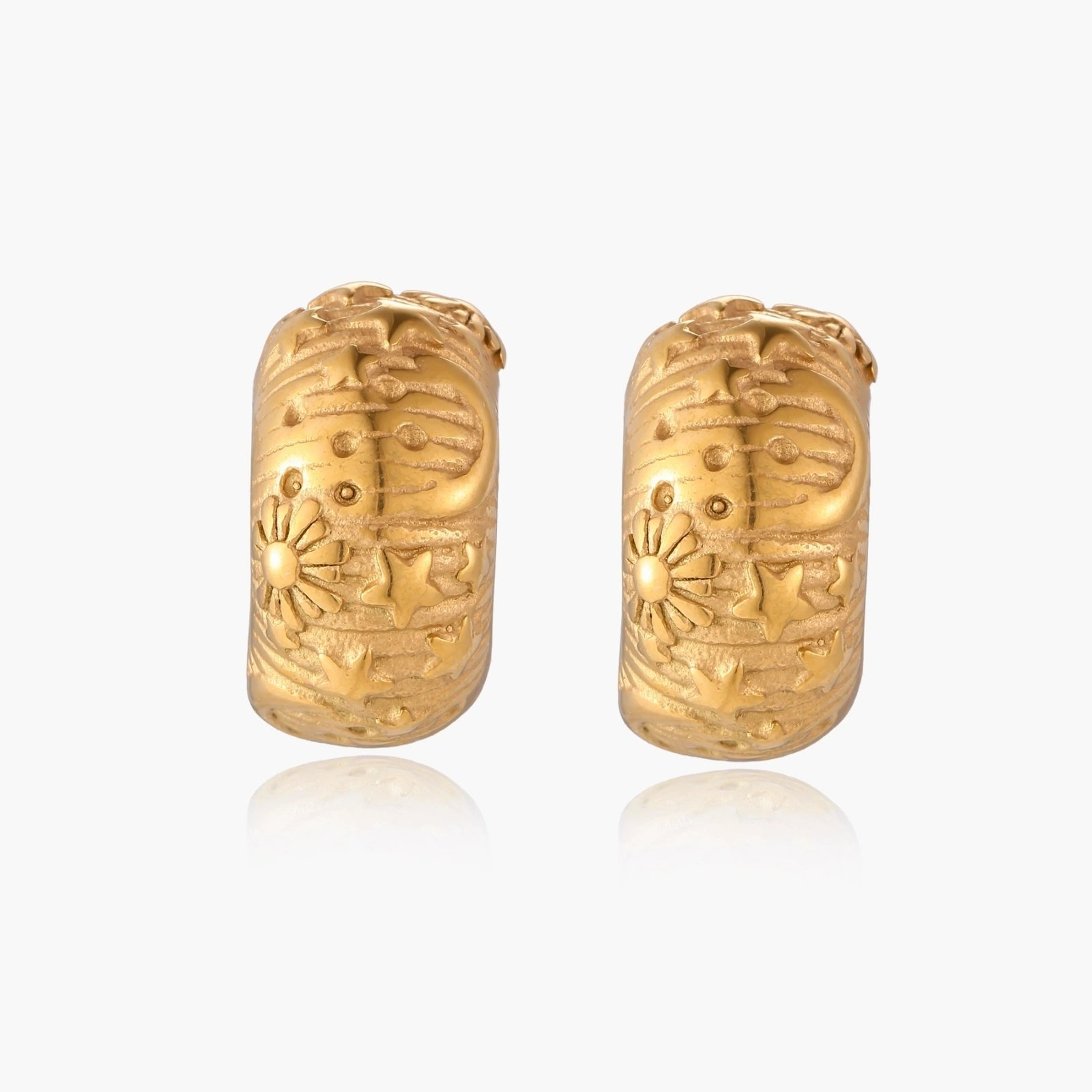 Wide gold hoop earrings with embossed stars and sun motifs on cream background, showing dimensional relief details.