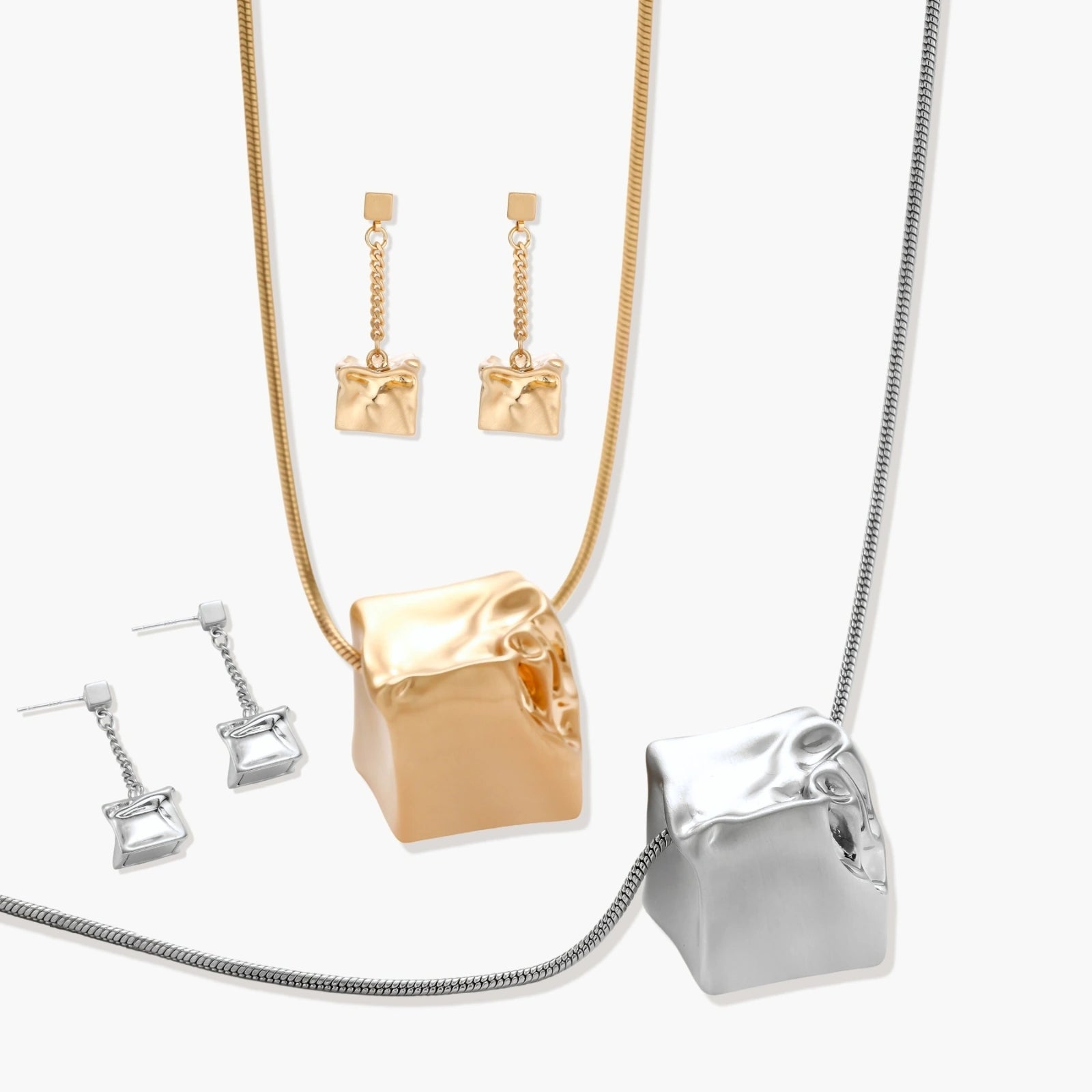 Modern geometric jewelry set featuring crumpled cube pendants in warm gold finish with chain details on beige background.