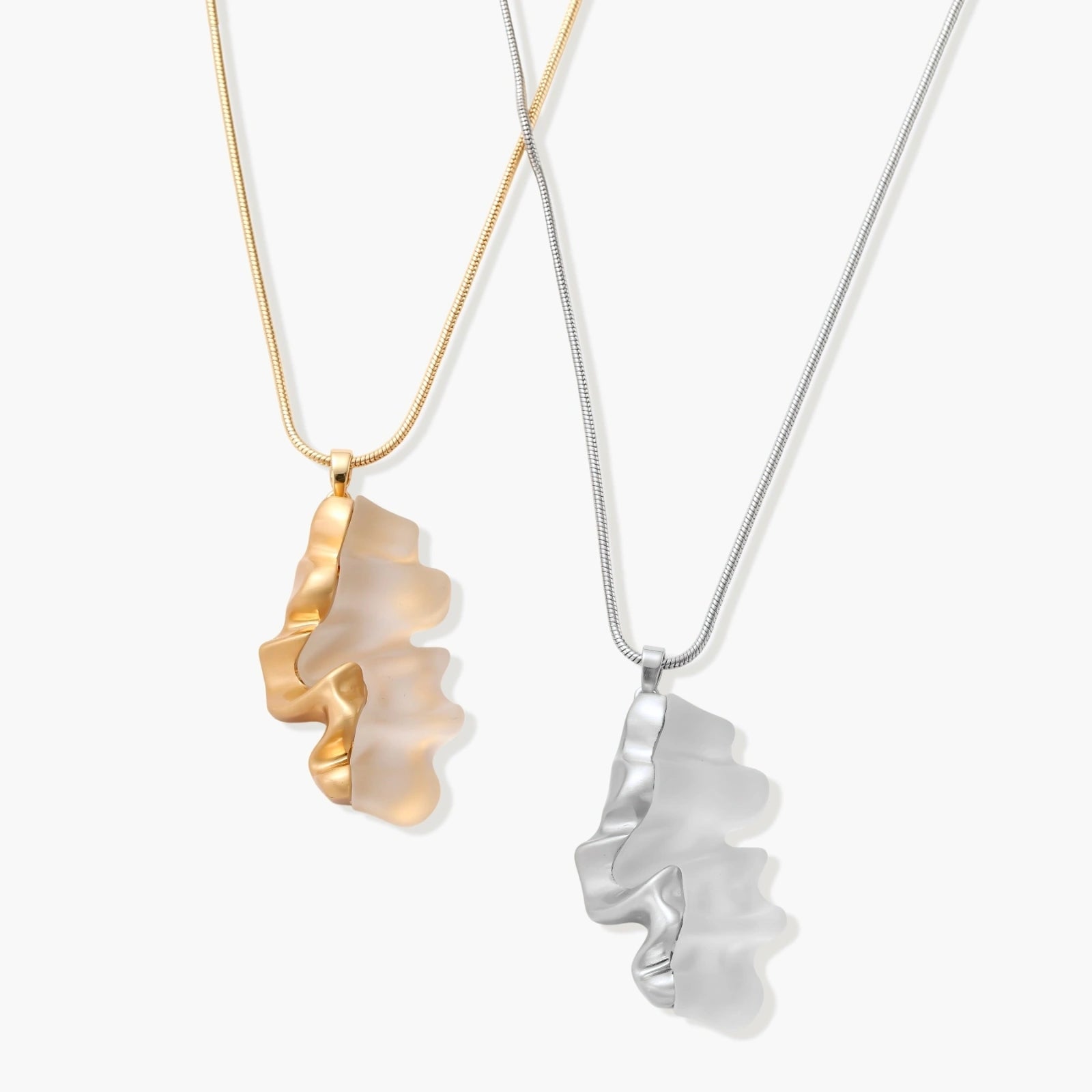 Modern sculptural pendant necklace with twisted metallic design on delicate silver chain against neutral background.